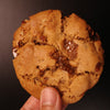 Hand holding a brown butter pecan cookie against a dark background