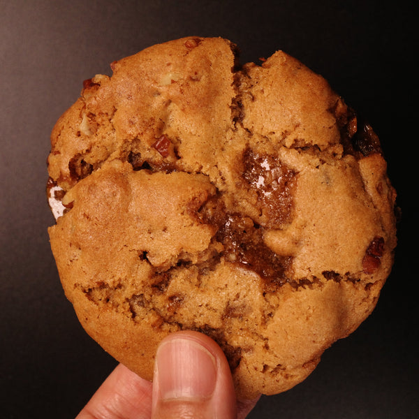 Hand holding a brown butter pecan cookie against a dark background